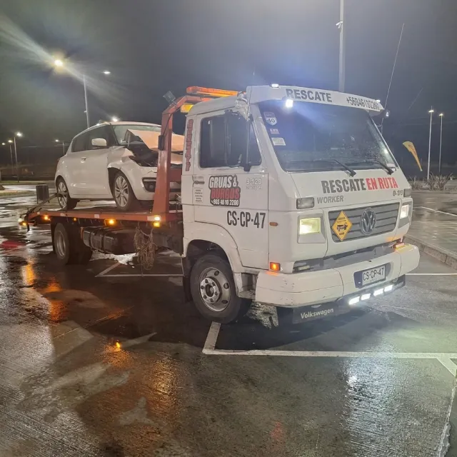 Grúa de noche en Villarrica con un auto chocado sobre la plataforma.